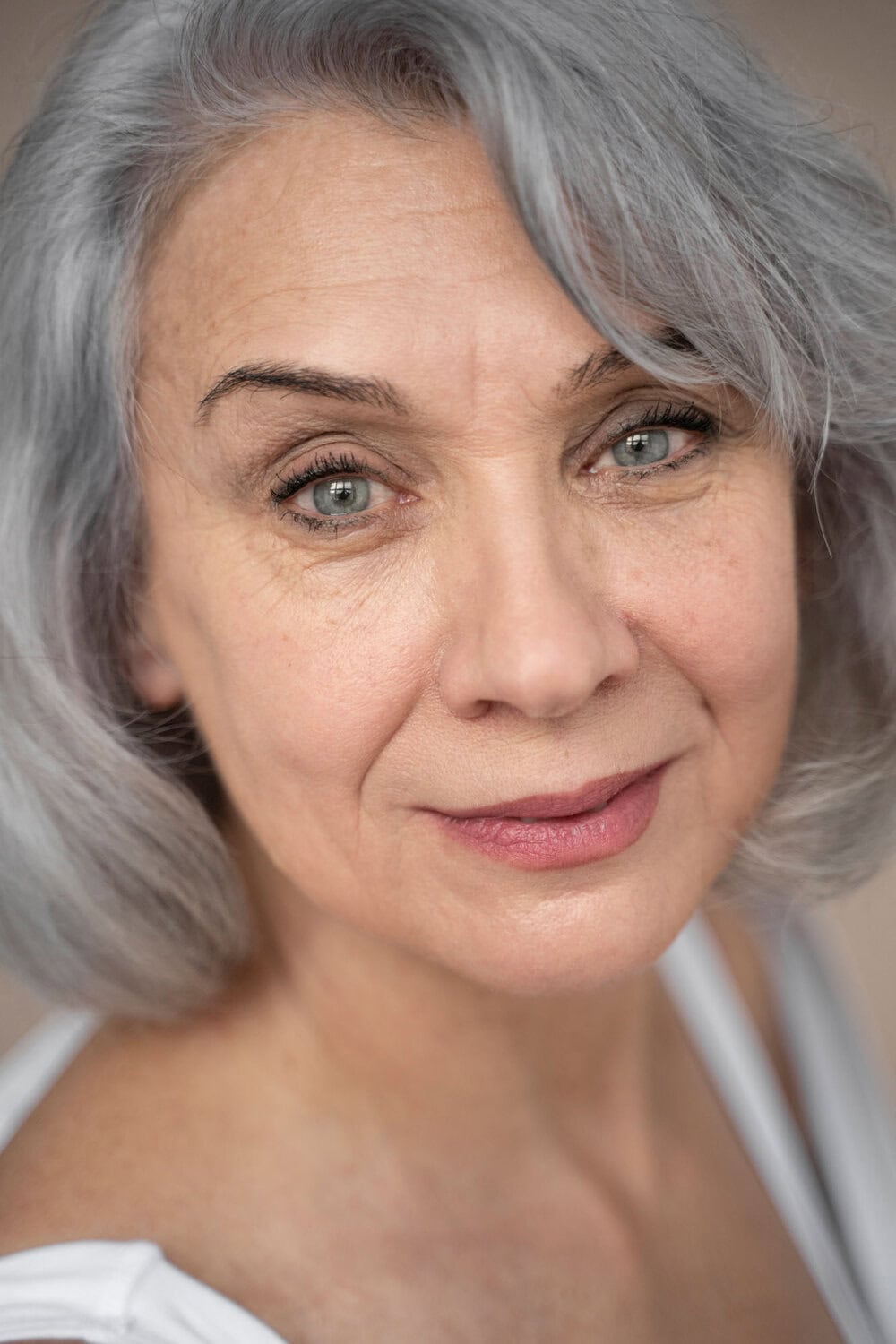 Leeftijdsloze vrouw met stralende huid en mooie grijze haar gebruikt cosmetische behandelingen bij Glow Clinic.
