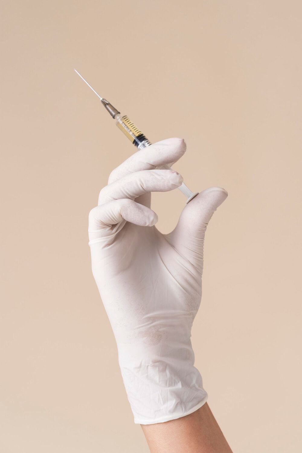Spuit met naald en handschoen, klaar voor huidbehandeling en cosmetische injecties.