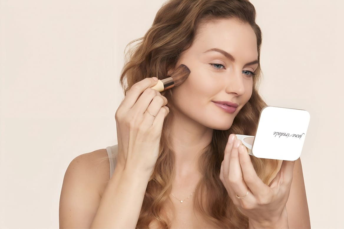 Stralende vrouw brengt make-up aan op haar gezicht met een kwast, huidverzorging en natuurlijke uitstraling.