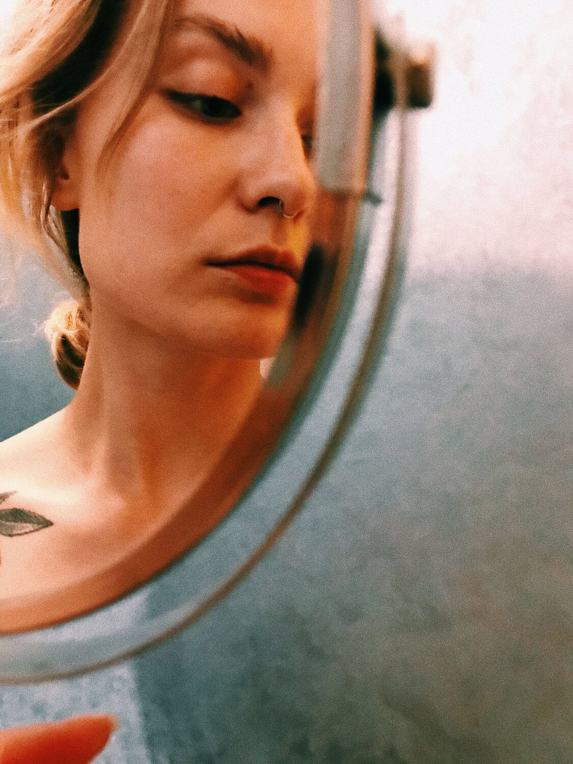 Zicht op een jonge vrouw, kijkend in een ronde spiegel, met een focus op haar huid- en haarverzorging.